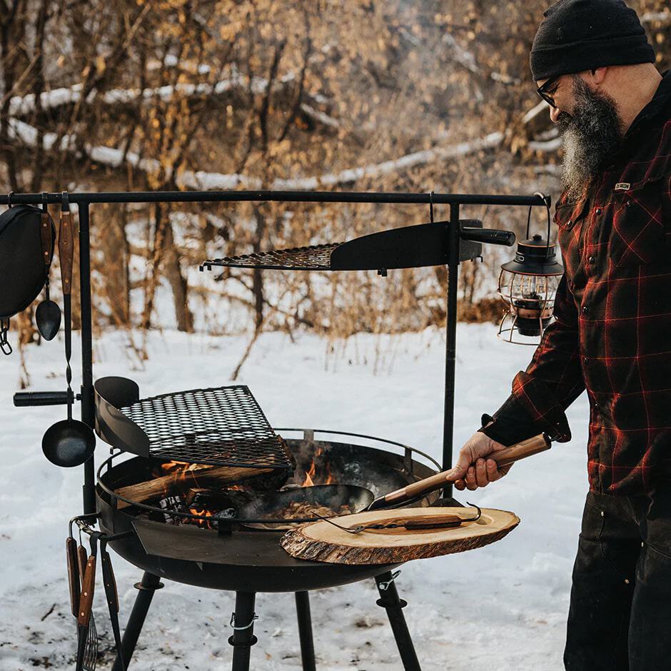 Man barbecueert buiten in de sneeuw met FØRSKELL outdoor uitrusting.